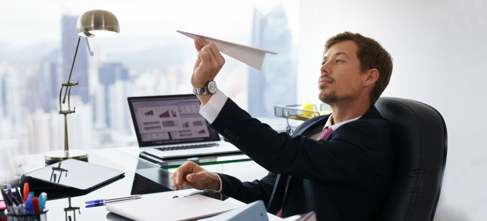 Businessman sitting at computer desk with laptop on but turned slightly away while aiming