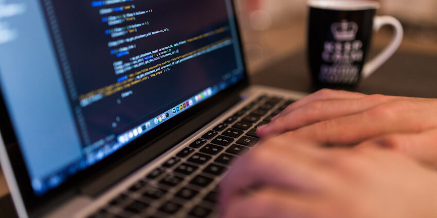 A closeup on someone's hands typing on a laptop computer; the screen shows code