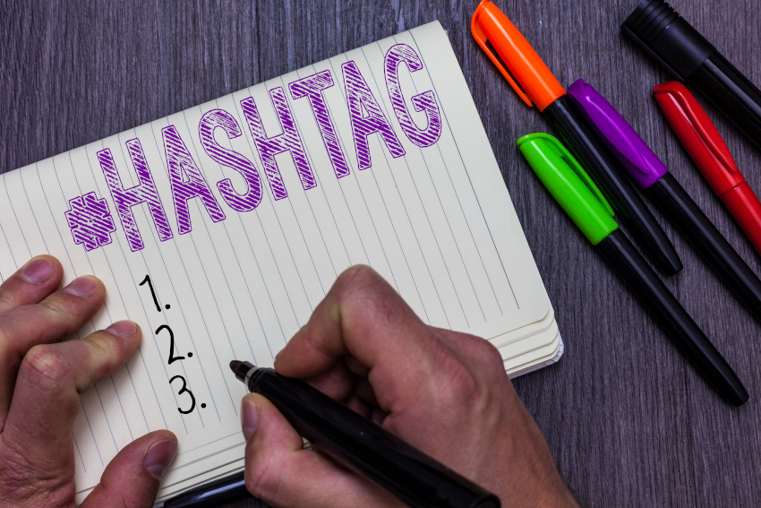 Person writing on a piece of lined paper with a marker, text: "#hashtag" and lists 1, 2, 3