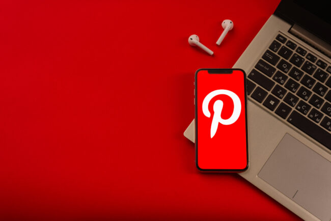smart phone sitting on top of a laptop keyboard, phone has red background & Pinterest logo on screen