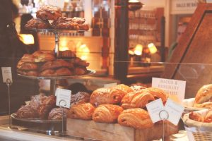 Display window of a bakery stuffed with a large amount of pastries, glazed and almond croissants, and bacon and rosemary fougasse.