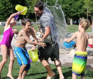 Group of smiling boys and girls dressed in bathing suits pouring water onto a counselor outside on a sunny day.