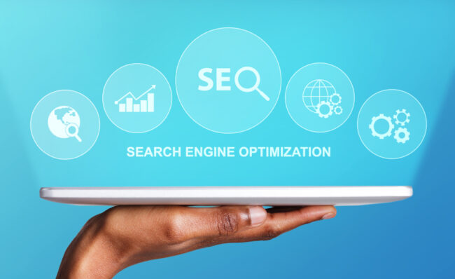 Search Engine Optimization, Male Hand Holding Digital Tablet With Seo Word And Seo-Optimization Tools Icons Over Blue Background.
