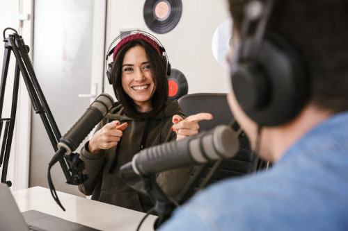 hosts smiling and talking into microphones while recording a podcast