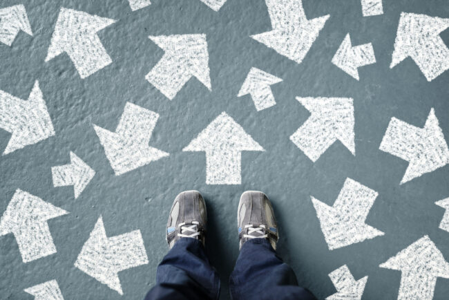 Top-down view of someone's tennis shoes while they stand in the middle of numerous arrows pointing all directions