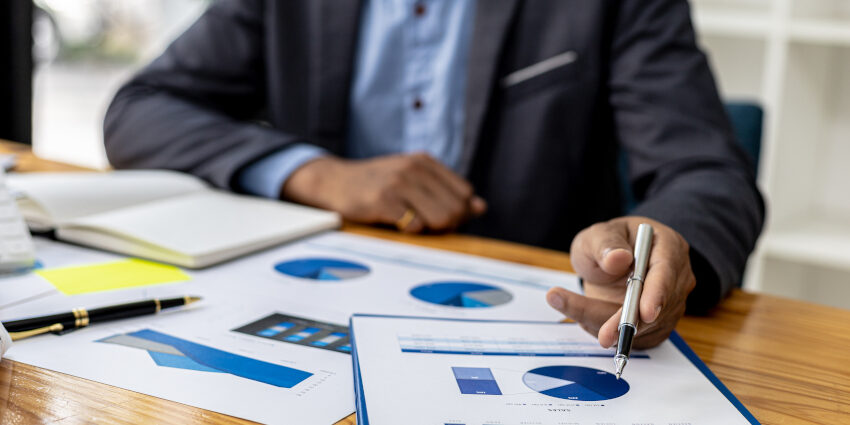 Businessman sits while studying papers on the desktop. The papers contain pie charts and other charts/graphs