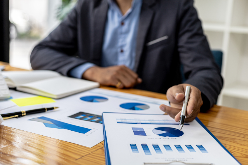 Businessman sits while studying papers on the desktop. The papers contain pie charts and other charts/graphs