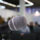 Close-up on microphone in the foreground with a large auditorium with people is in the background.