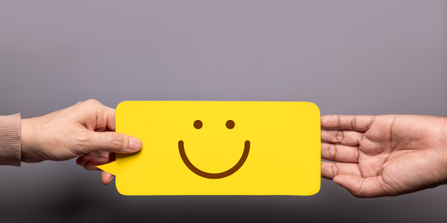 A hand is grabbing a yellow-colored text bubble with a smiley face as a second person's hand lets go