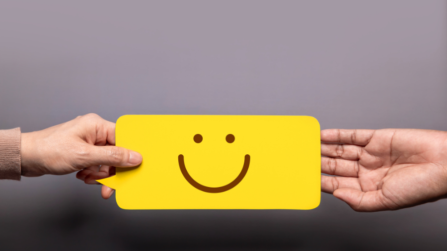 A hand is grabbing a yellow-colored text bubble with a smiley face as a second person's hand lets go