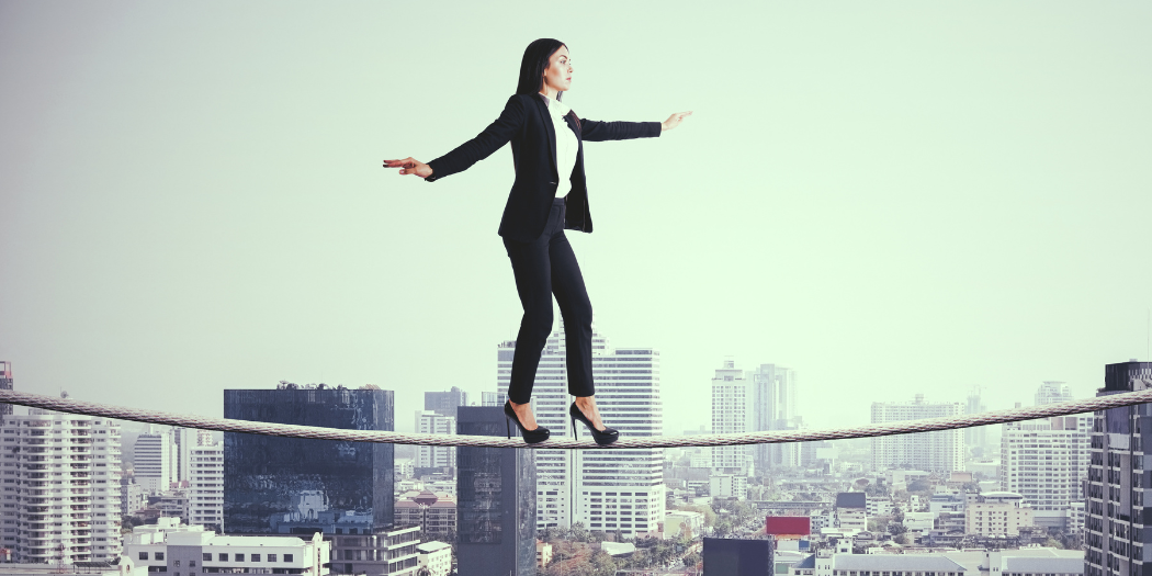business woman walking on a high wire with tall city buildings in the background