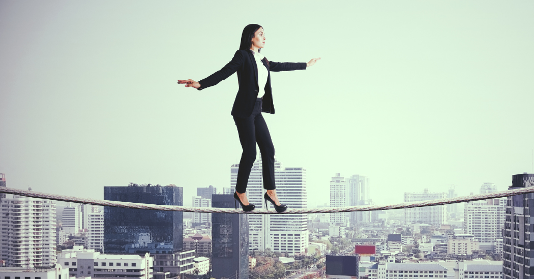 business woman walking on a high wire with tall city buildings in the background