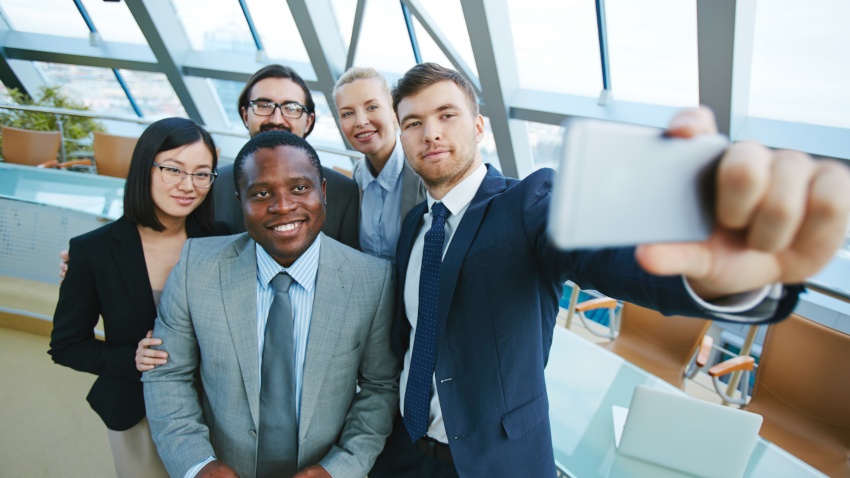 Group of adults dressed in business attire smile for a selfie
